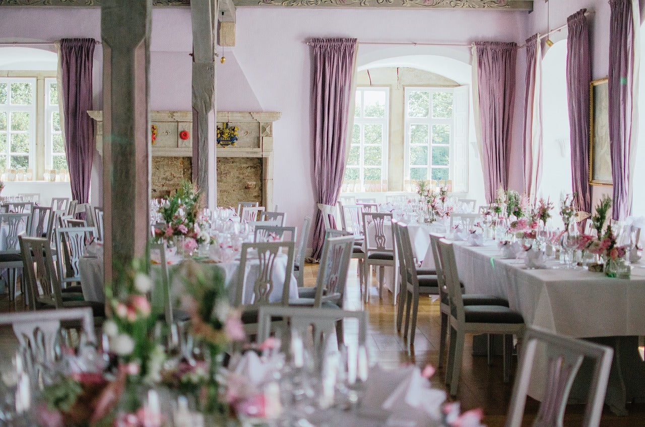 Kuvassa on pinkillä ja valkoisella koristeltu juhlapaikka, joka on jaettu pöytäryhmiin.