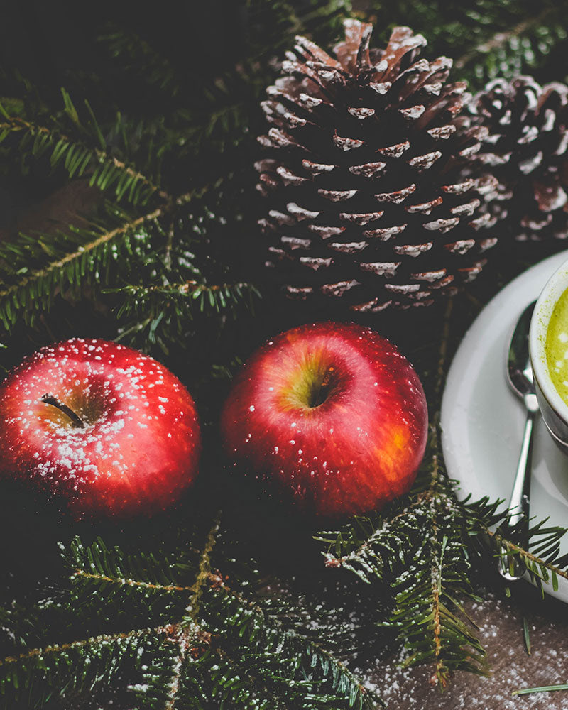 Omenoita, käpy ja kuusenoksa pöydällä. 