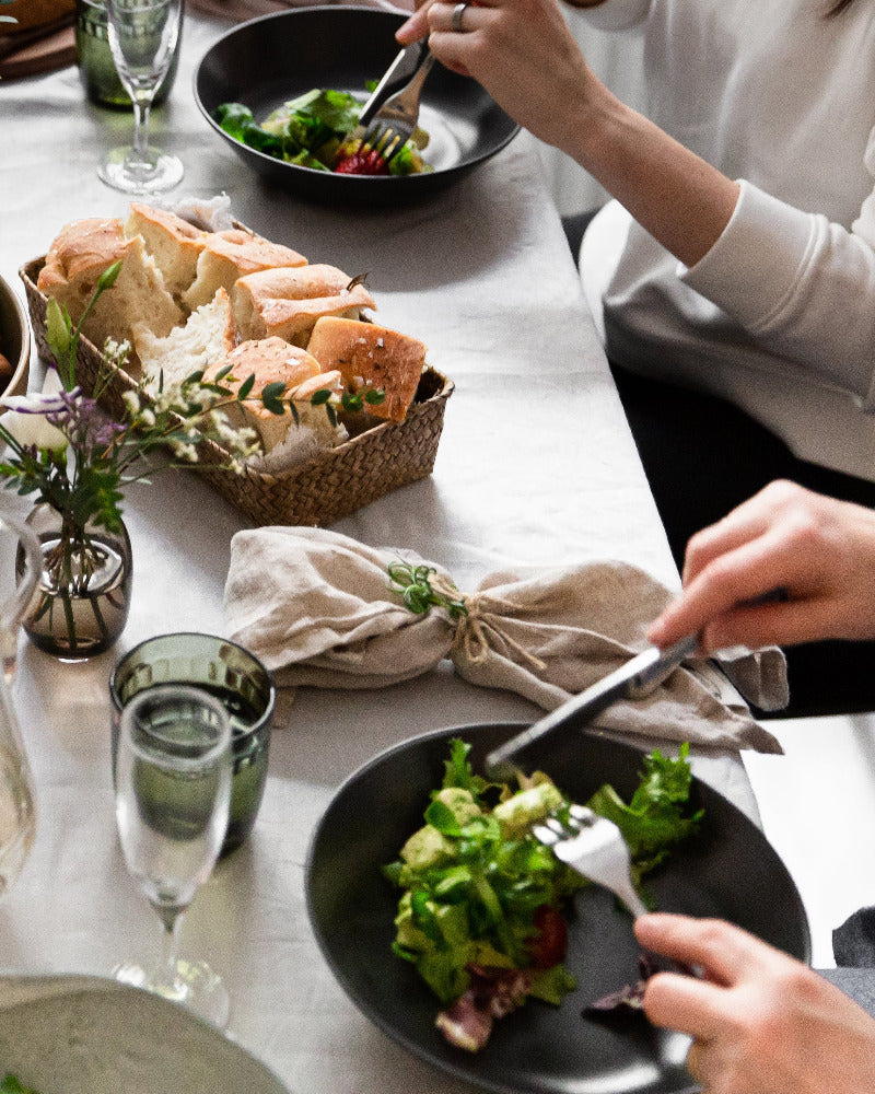 Kesäinen lounashetki, lounastajien lautasilla salaattia, pellavaliinat, kesäkukkia ja foccacciaa.