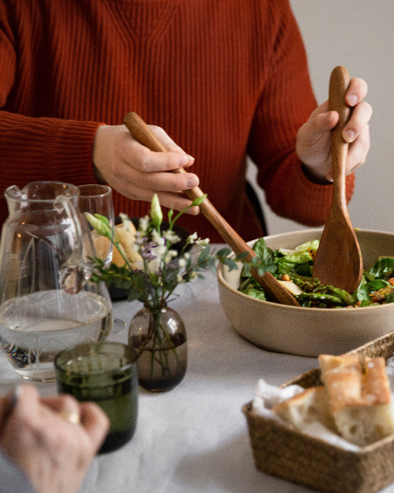 Lounassalaatti ja foccacciaa katettuna valkoiselle pellavaliinalle, neuleeseen pukeutunut lounastaja annostelee salaattia.