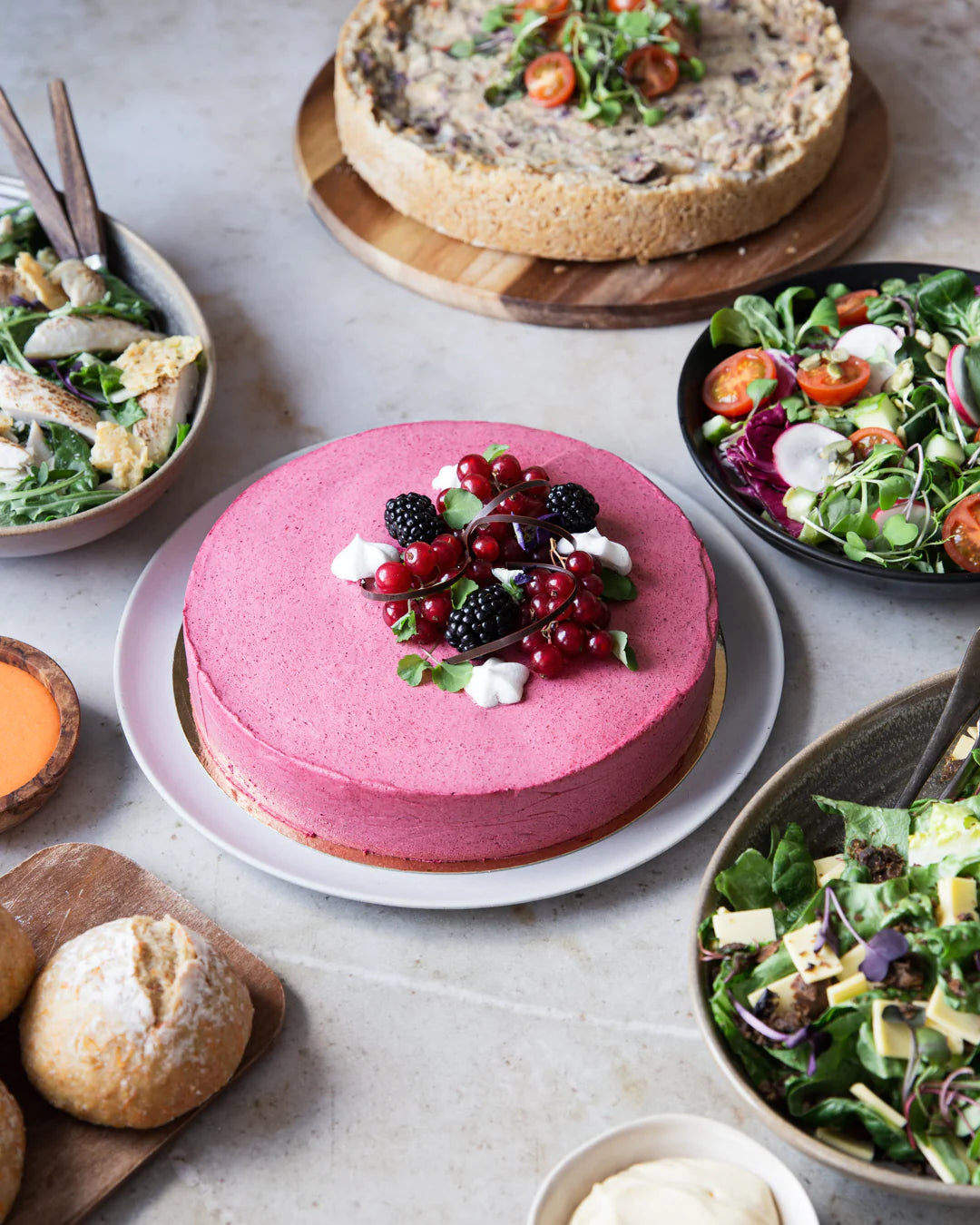 Juhlava kattaus, jossa marjainen juustokakku ja suolaisia alkupaloja salaateilla ja piirakalla. 