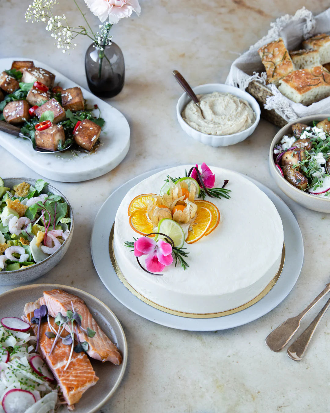 Juhlava kattaus, jossa valkoinen juustokakku ja suolaisia alkupaloja salaateilla. 