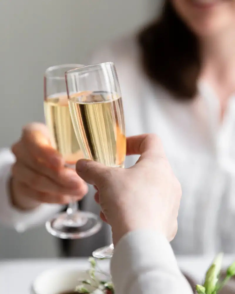 Kaksi henkilöä kilistää kuohuviinilaseja. 