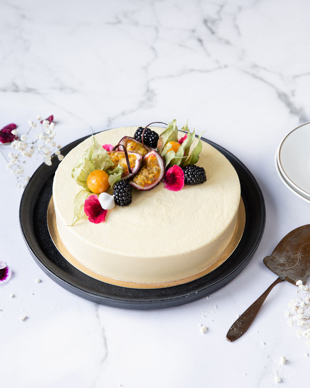 Passionhedelmällä, marjoilla ja kukilla koristeltu passionmoussekakku. 