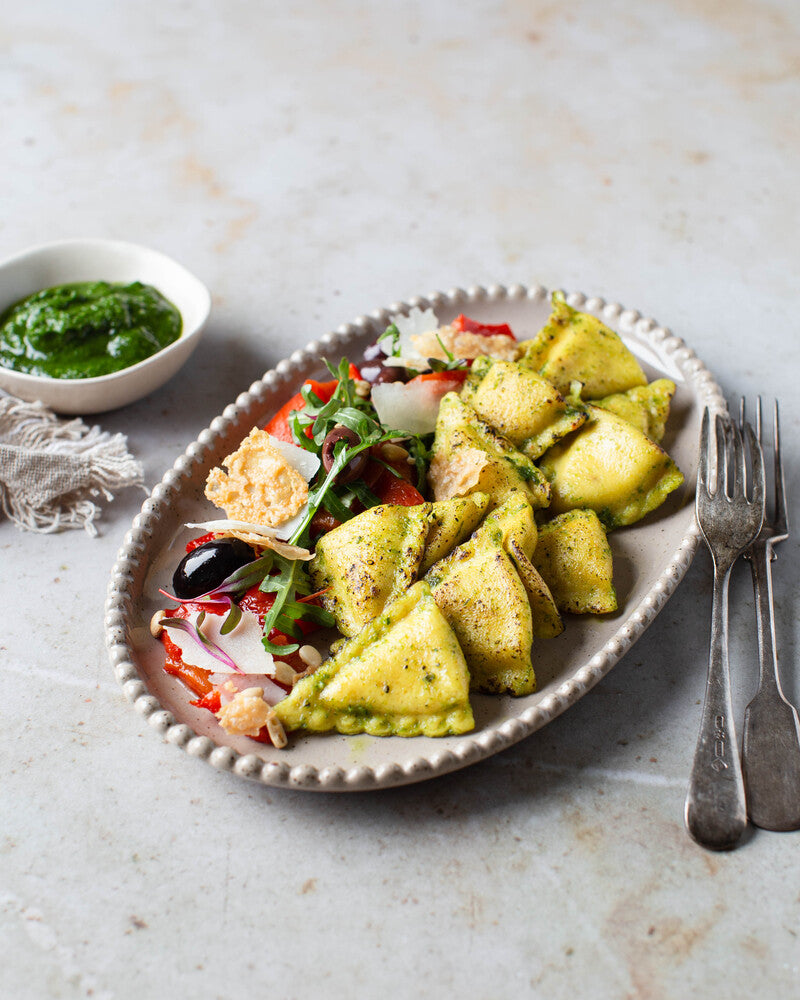 Tomaatti-provoloneravioleja ja pestopaahdettuja kasviksia tarjoiluastialla.