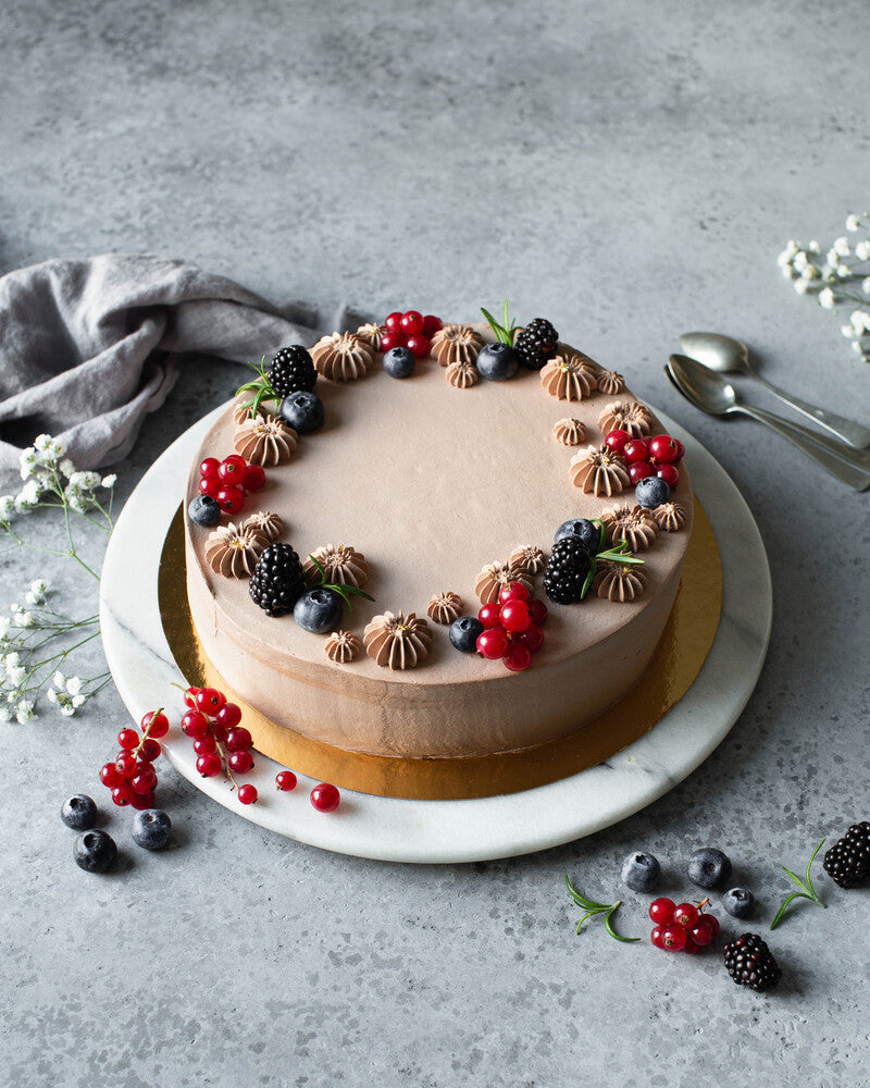 Mustikoilla ja karhunvatukoilla koristeltu suklaa-passionmoussekakku tarjoilulautasella. 