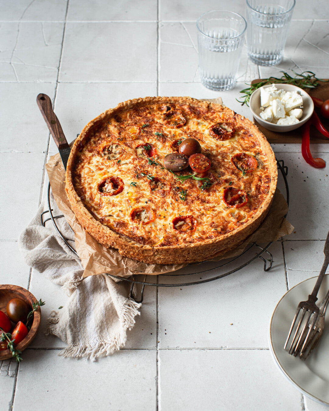 Kirsikkatomaateilla koristeltu välimerellinen fetapiirakka tarjoiluastialla.