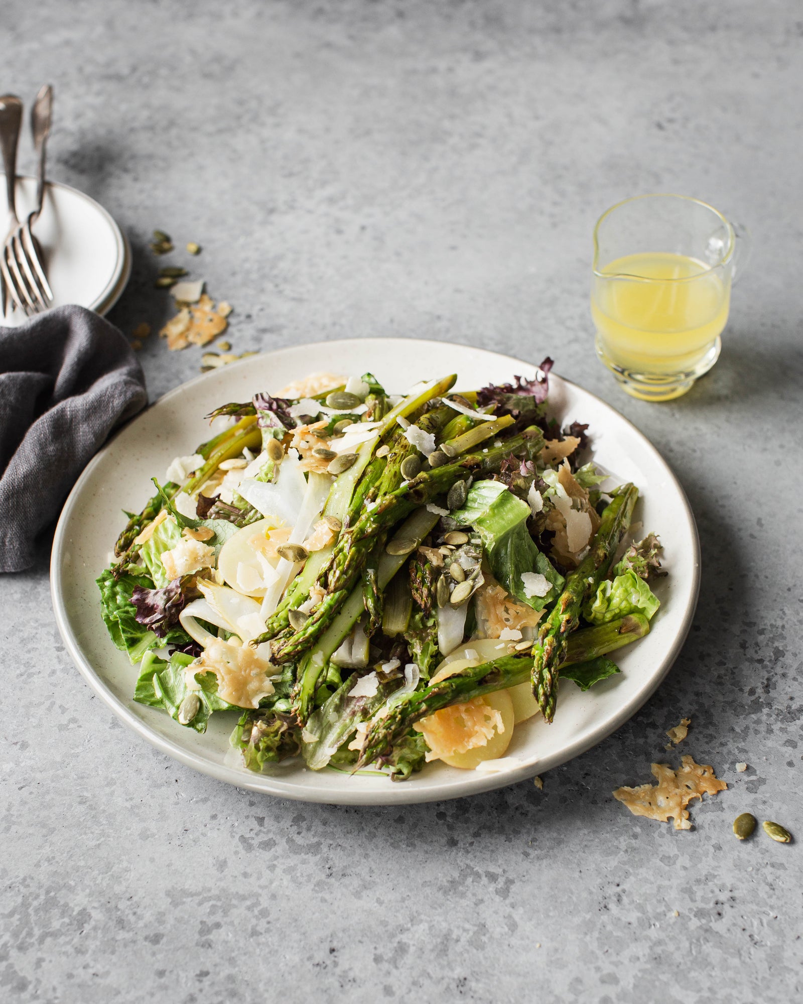 Keväistä parsa-parmesaanisalaattia ja limevinaigrettea tarjoiluastialla.