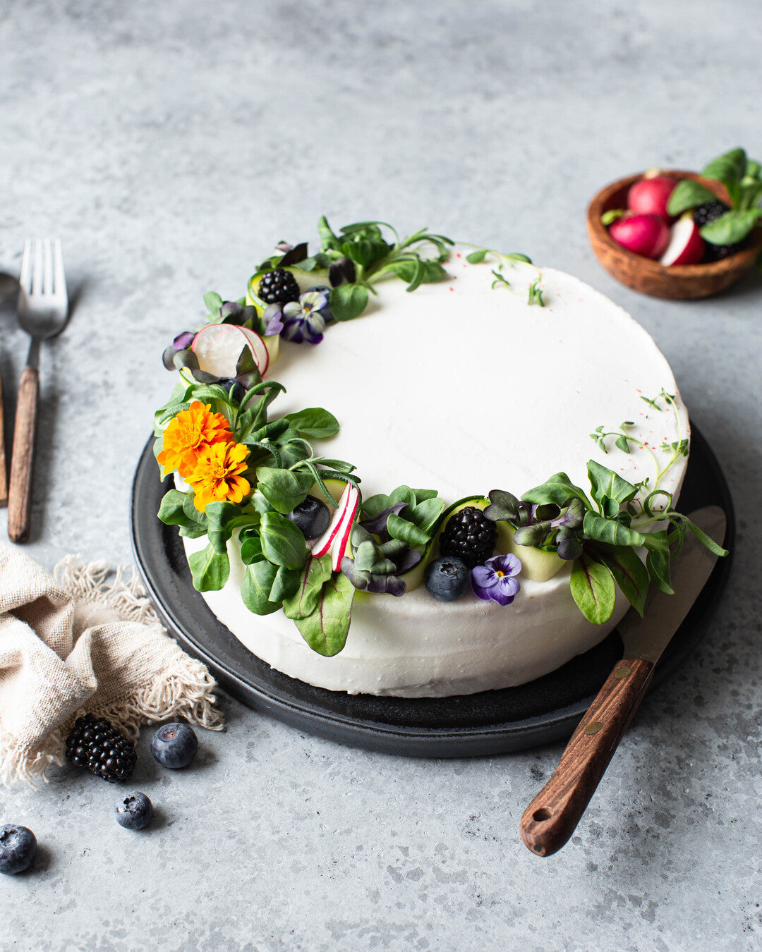 Vuonankaalilla ja kukilla koristeltu nyhtöhernevoileipäkakku tarjoiluastialla.