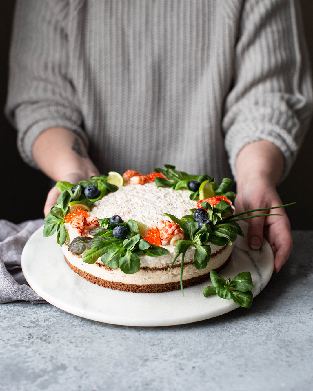 Vuonankaalilla, katkaravulla ja mustikoilla koristeltu saaristolaisvoileipäkakku tarjoiluastialla.