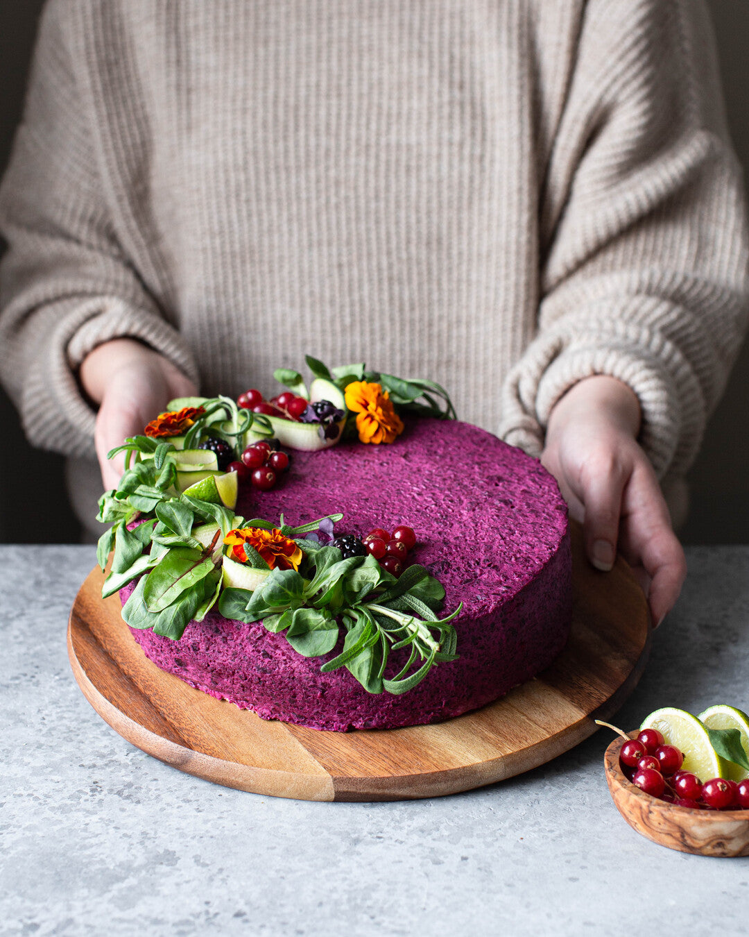 Värikäs vuonankaalilla koristeltu vuohenjuusto-punajuurivoileipäkakku tarjoiluastialla.